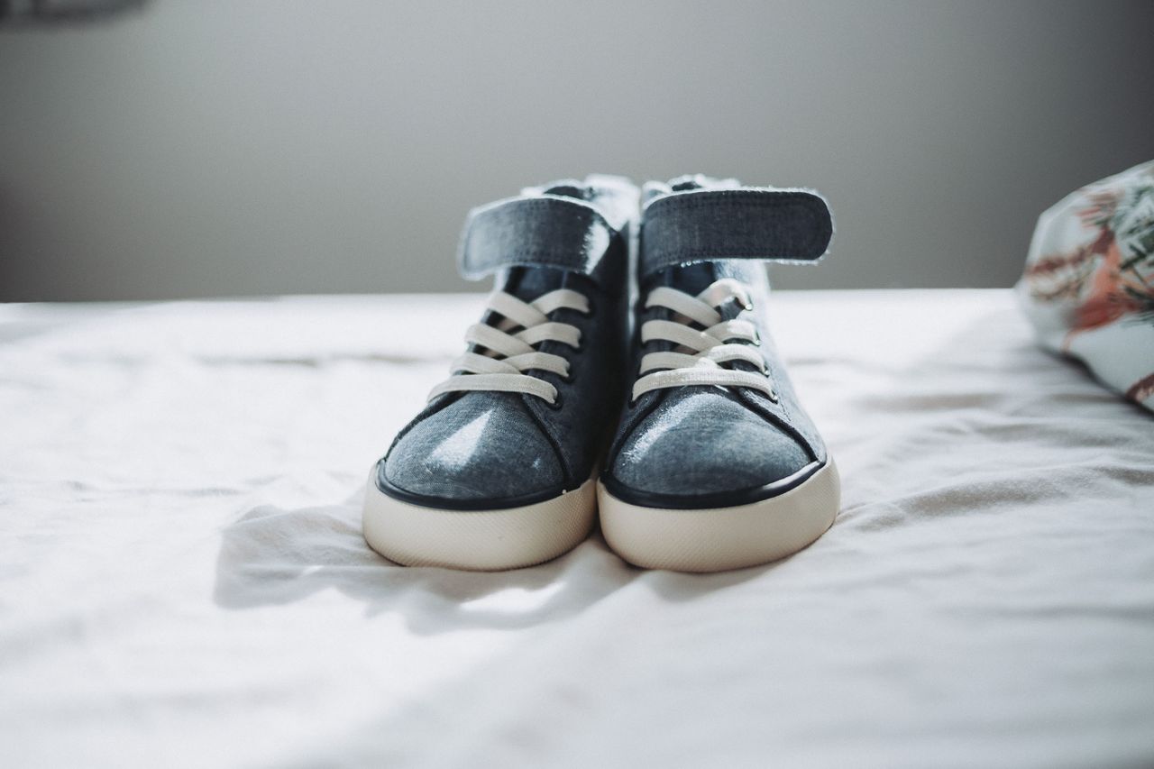 our-journey-02 Close-up of trendy denim sneakers on a bed, perfect for fashion enthusiasts.