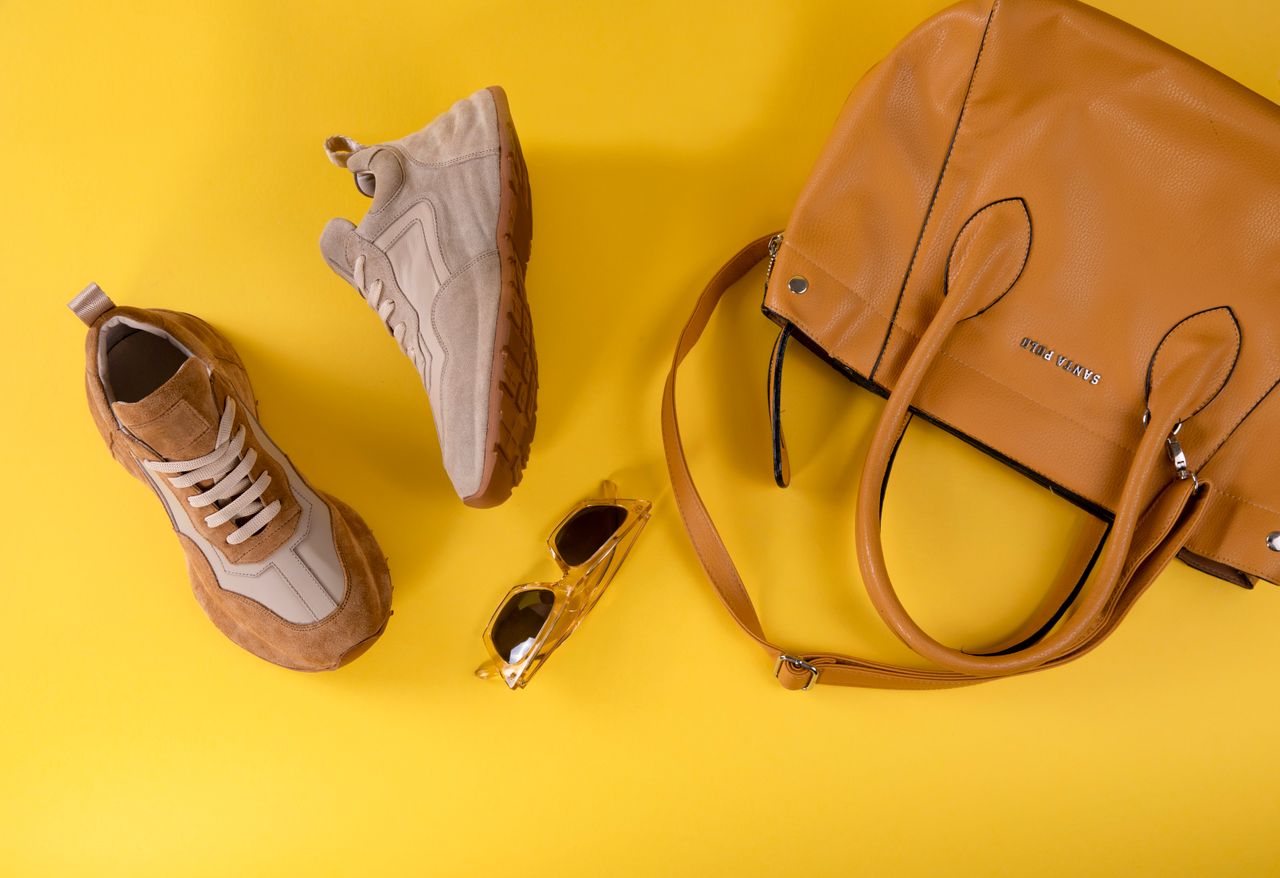 experience-img Stylish brown handbag, fashionable eyewear, and sport shoes on vibrant yellow background.