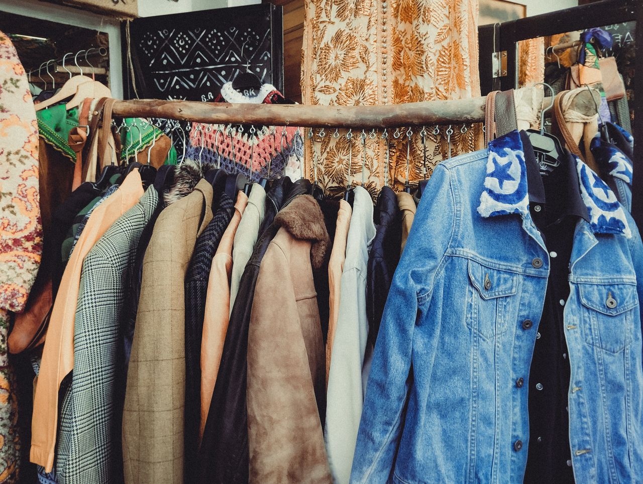 who-we-are-img A vibrant assortment of vintage jackets hanging on a wooden rack in a boutique.